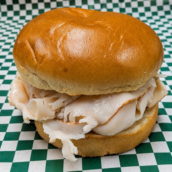 A turkey sandwich on a bun, filled with thinly sliced turkey, on green and white checkered paper.