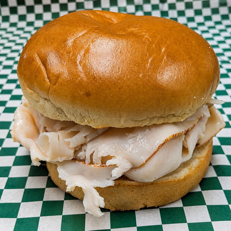A turkey sandwich on a bun, filled with thinly sliced turkey, on green and white checkered paper.