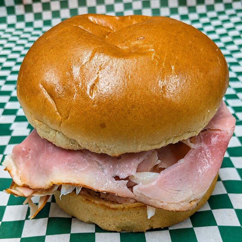 A ham and cheese sandwich on a brioche bun, resting on a green and white checkered paper.