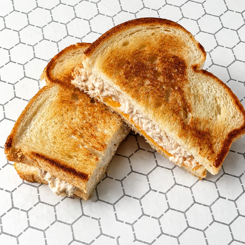 Two halves of a grilled tuna melt sandwich with cheese on toasted bread, on a hexagonal pattern surface.